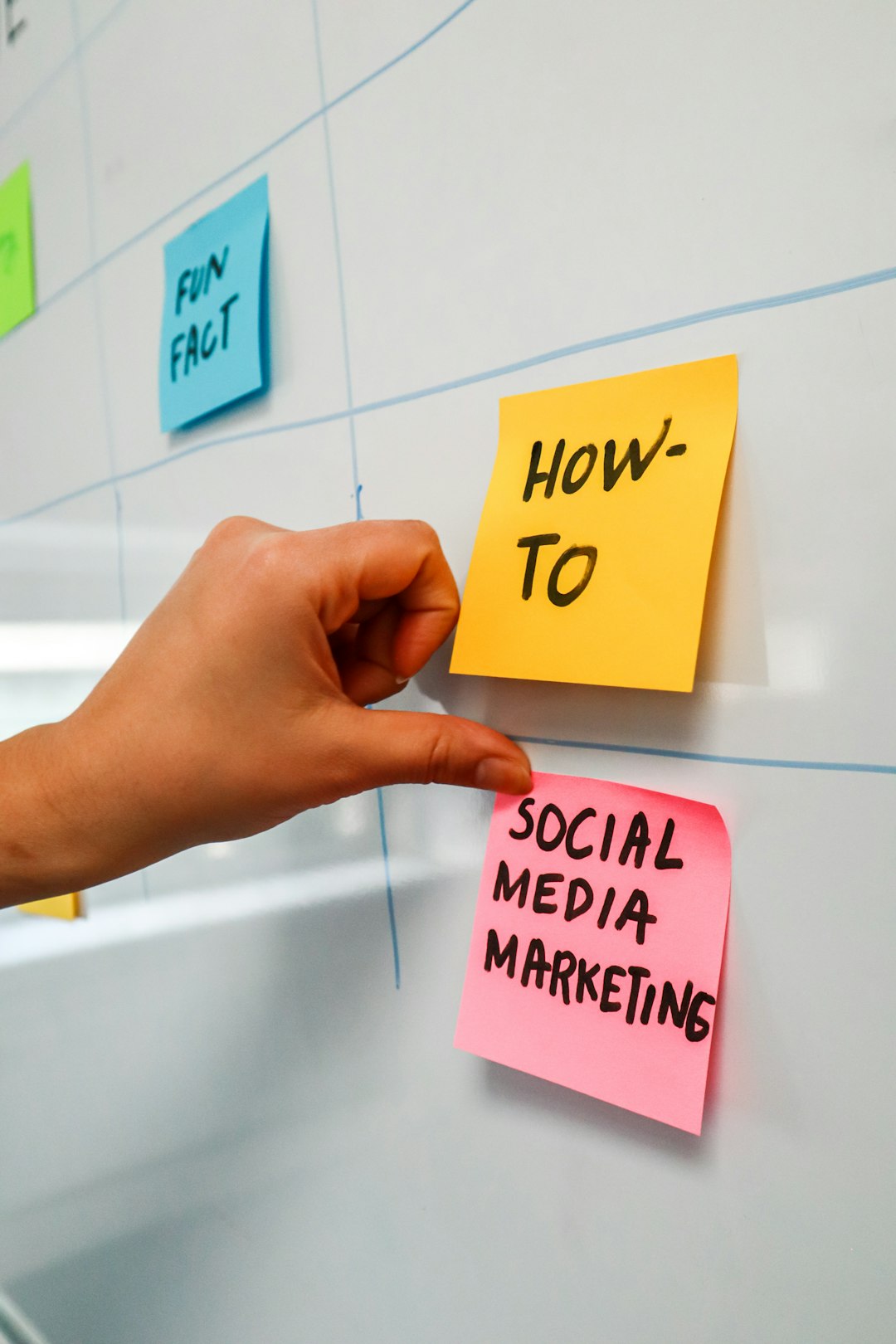 Personne en train d’apposer un post-it sur un tableau blanc portant les mots Social Media Marketing